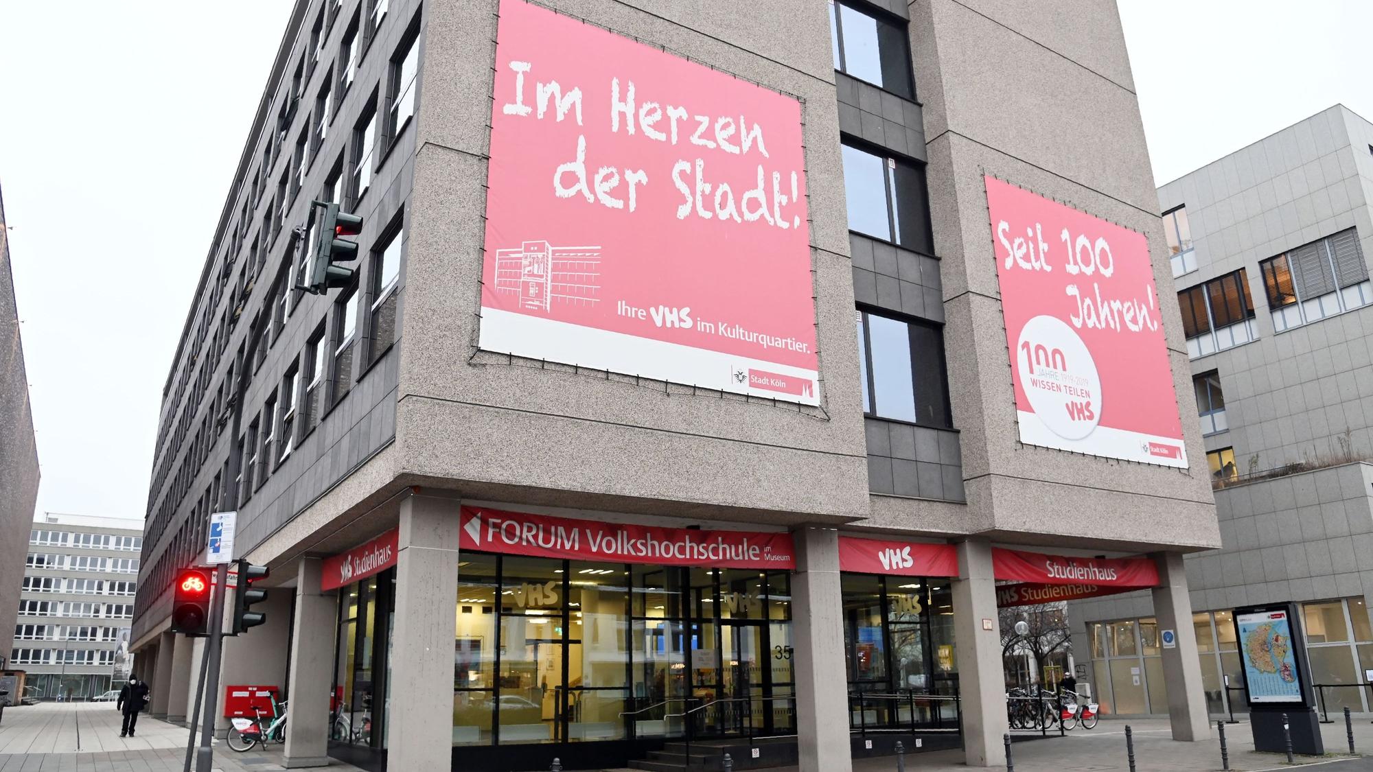 An der Fassade des Gebäudes der Volkshochschule in Köln hängt ein großes, rotes Werbeplakat, auf dem zu lesen steht "Im Herzen der Stadt".