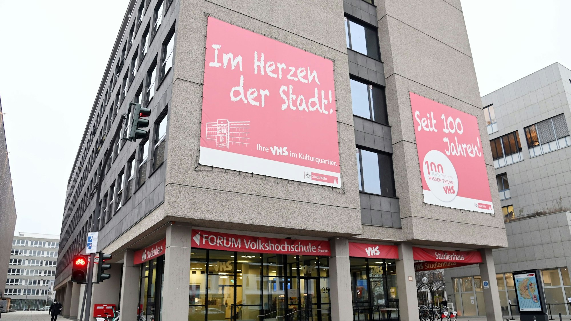 Das Gebäude der Volkshochschule in Köln, auf Plakaten an der Wand steht: „Im Herzen der Stadt!“ und „Seit 100 Jahren!“.