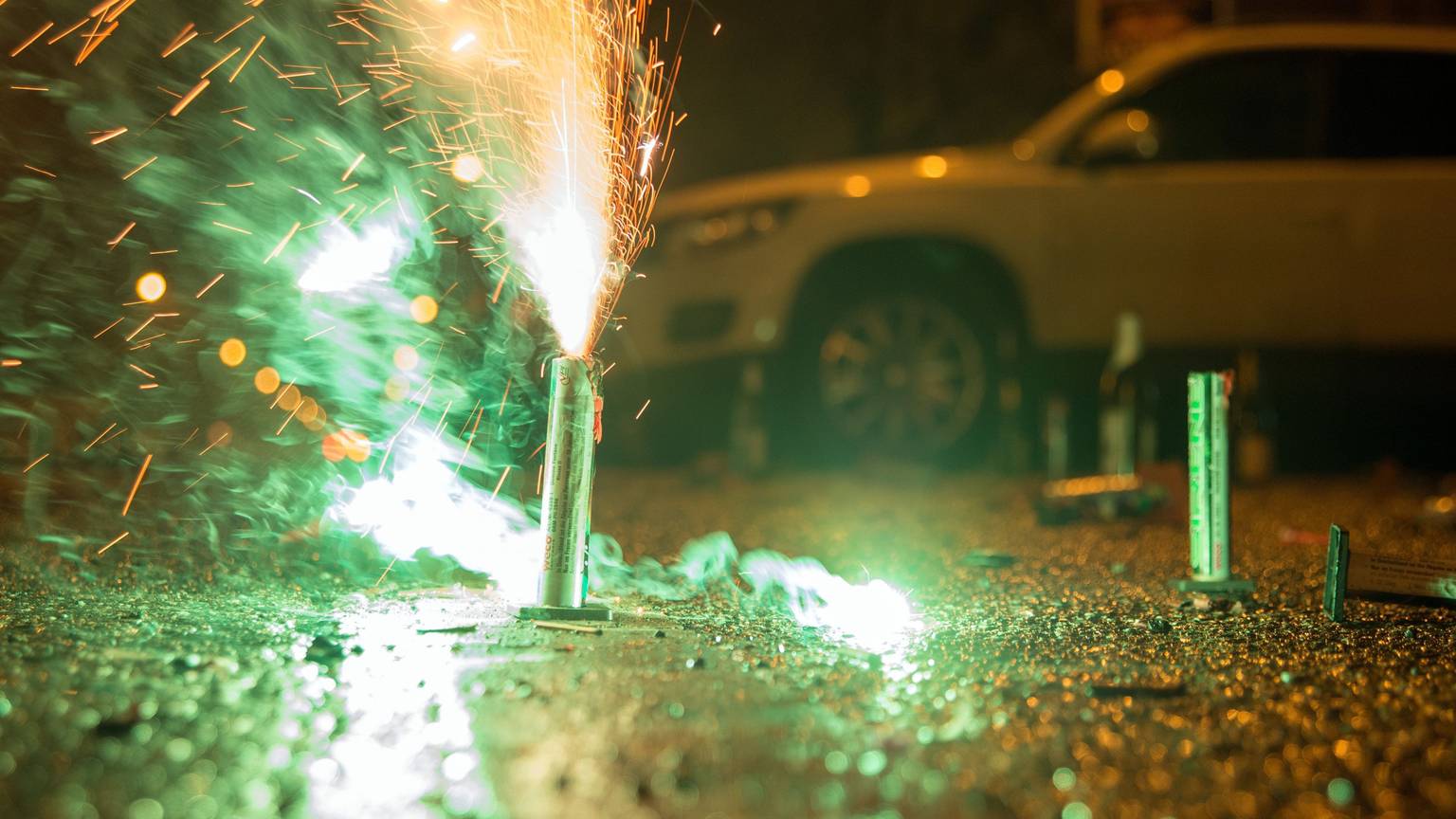 Ein Feuerwerkskörper sprüht Funken vor einem geparkten Auto.