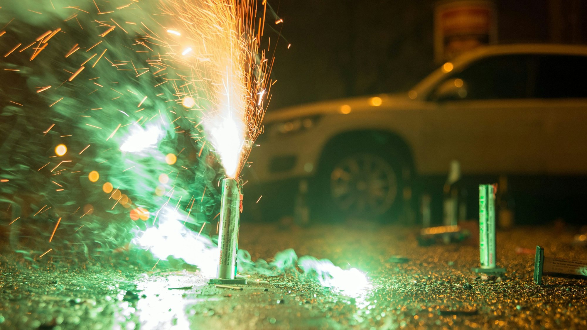 Ein Feuerwerkskörper sprüht Funken vor einem geparkten Auto.