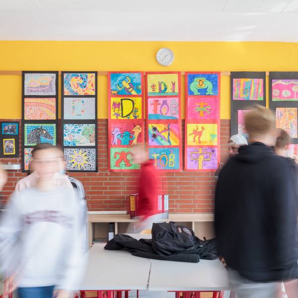 Schülerinnen und Schüler in einem Klassenzimmer mit bunten Bildern an den Wänden. Die Kinder sind verschwommen fotografiert und unkenntlich.