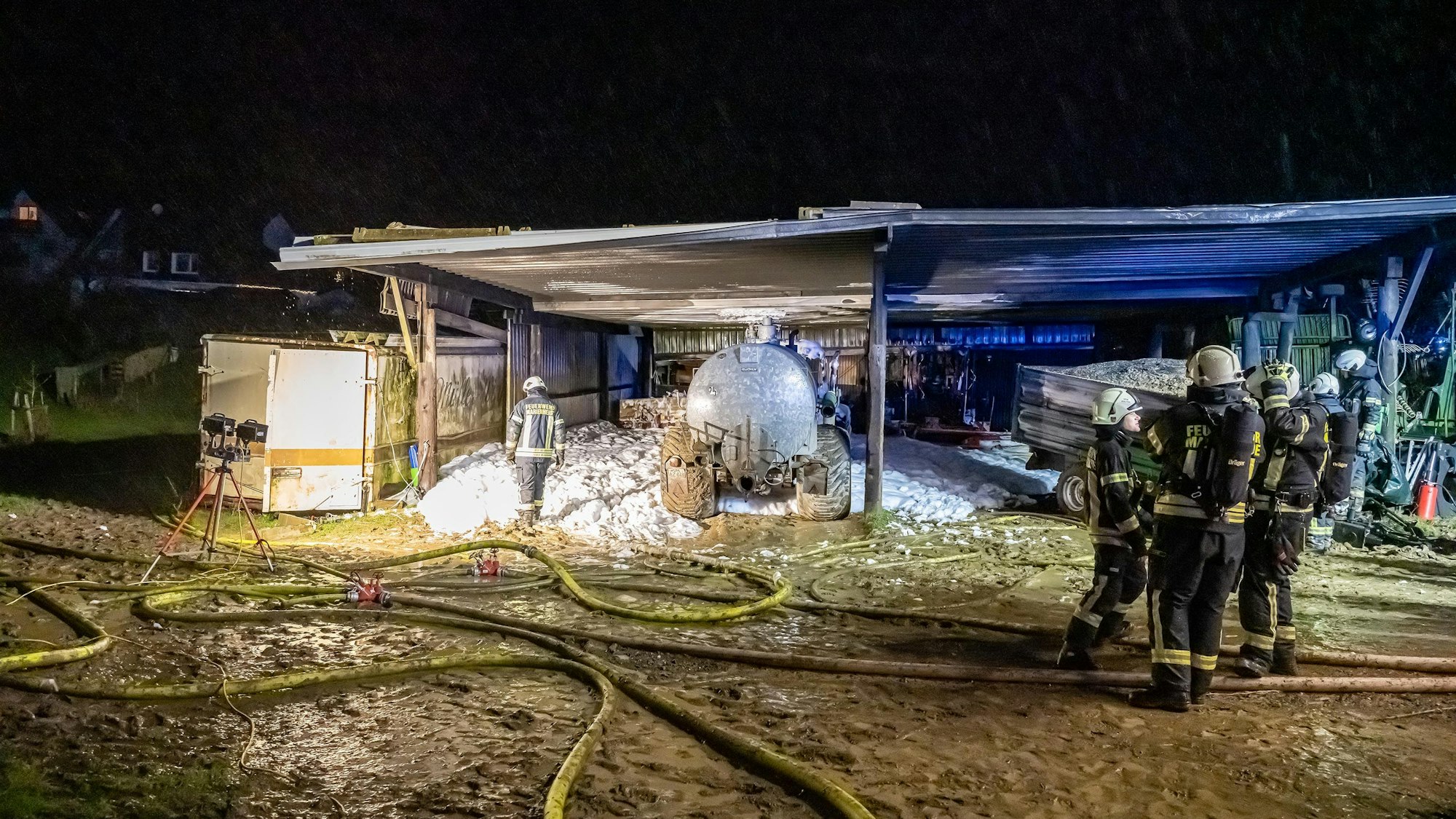 Zu sehen ist ein ausgebrannter Traktor mit angehängtem Güllefass in einem Unterstand.