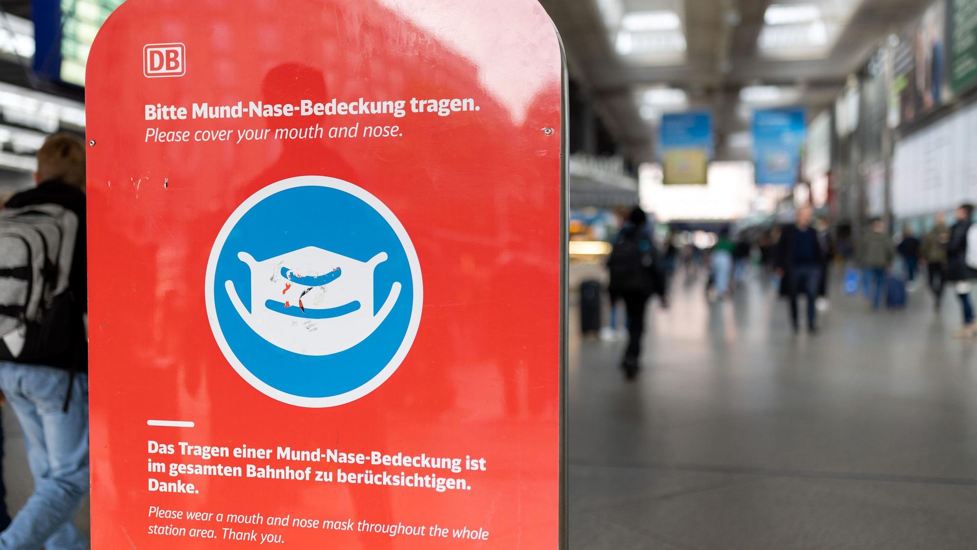 Ein Schild mit der Aufschrift „Bitte Mund-Nase-Bedeckung tragen!“ steht auf einem Schild am Eingang im Hauptbahnhof.
In den Fernzügen der Bahn gilt noch immer die Maskenpflicht.
