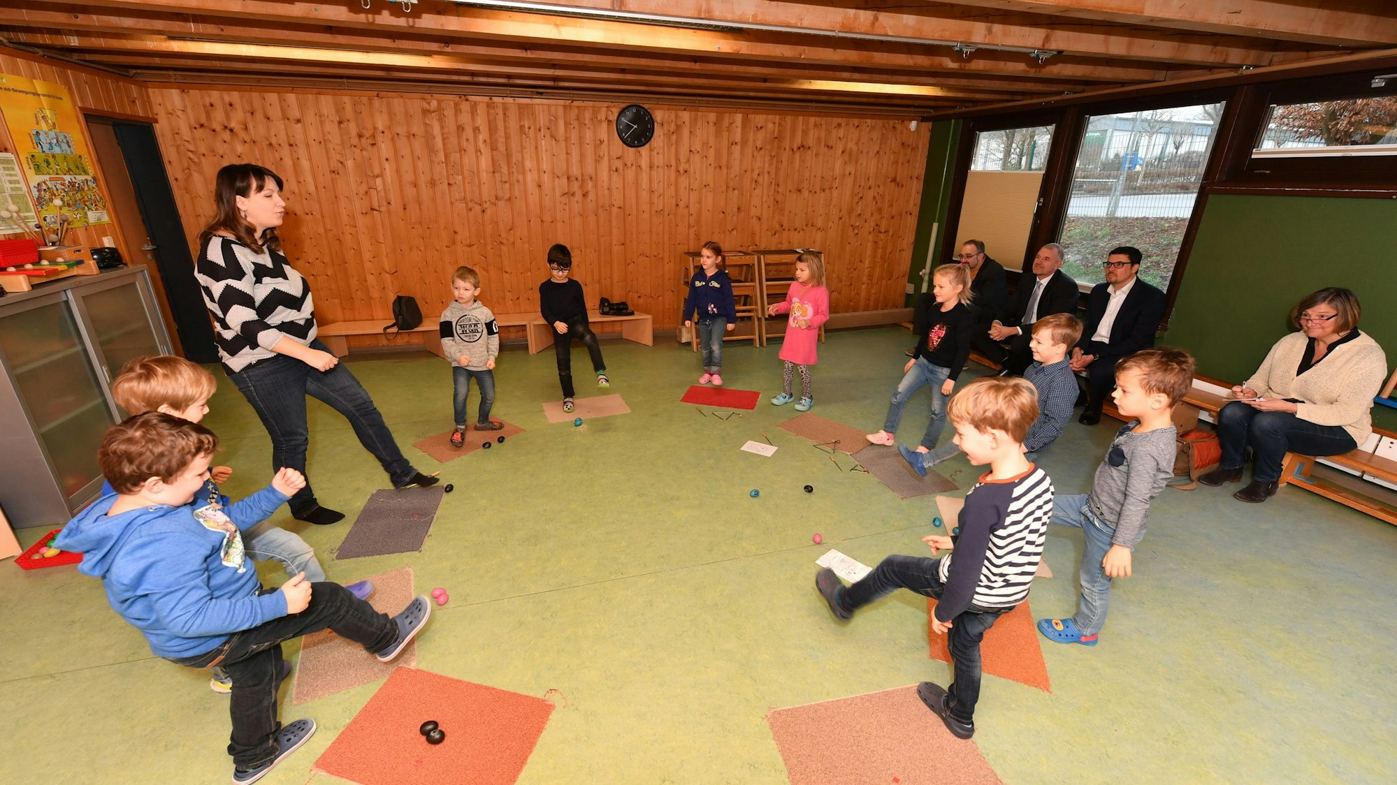 Kinder und eine Erzieherin stehen in einem Kreis und heben ihre Beine.