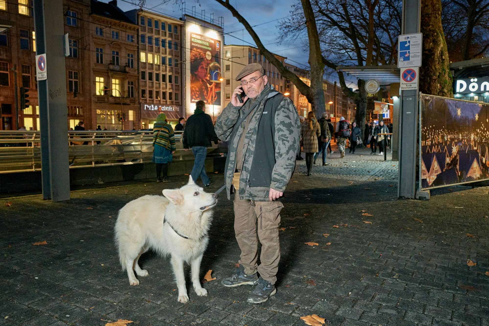 Franco Clemens steht mit Handy am Ohr vor dem Neumarkt, daneben sein Hund Bowie.