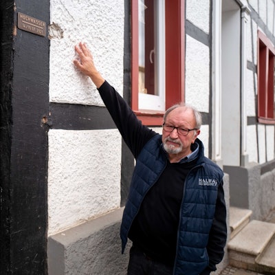 Robert Zimmermann zeigt an seinem Haus in Arloff, wie hoch das Wasser während der Flut 2021 stand. Dort ist auch eine Plakette angebracht worden, die das historische Hochwasser dokumentiert.