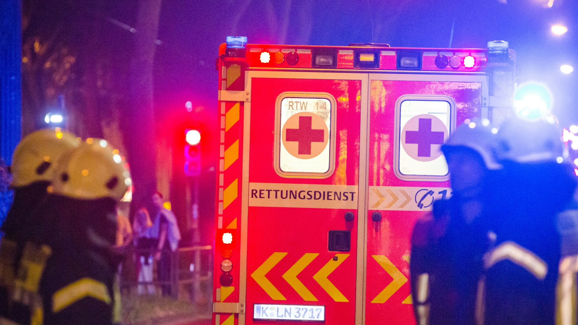 Ein Rettungswagen steht vor mehreren Feuerwehrleuten an einer Einsatzstelle in Köln. (Symbolbild)