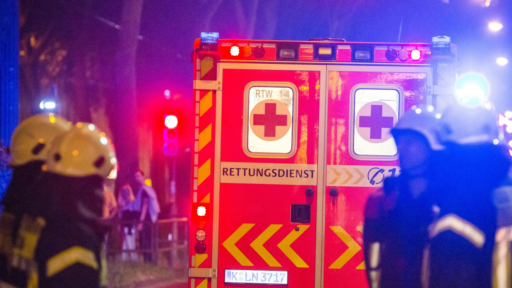 Ein Rettungswagen steht vor mehreren Feuerwehrleuten an einer Einsatzstelle in Köln. (Symbolbild)