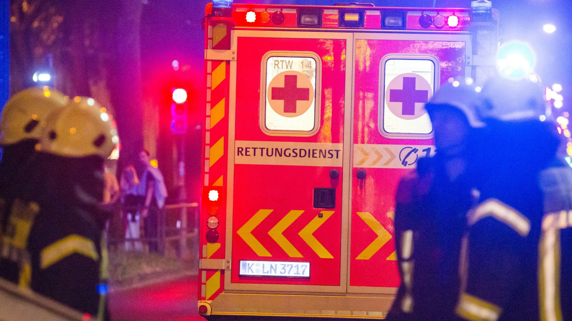 Feuerwehrleute stehen nachts hinter einem Rettungswagen.