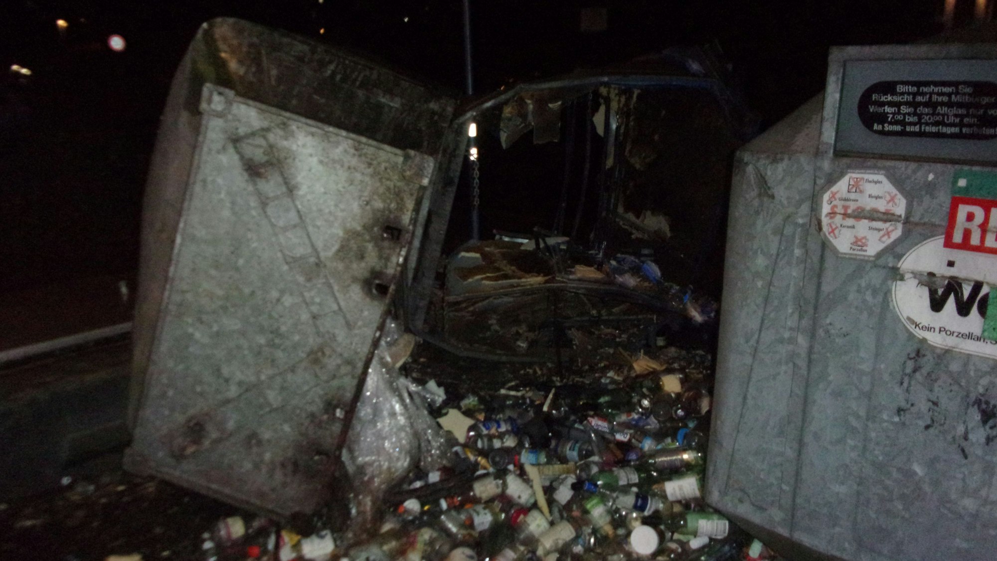 Glasflaschen und Gläser liegen neben dem Container, der durch die Explosion schwer beschädigt worden ist.