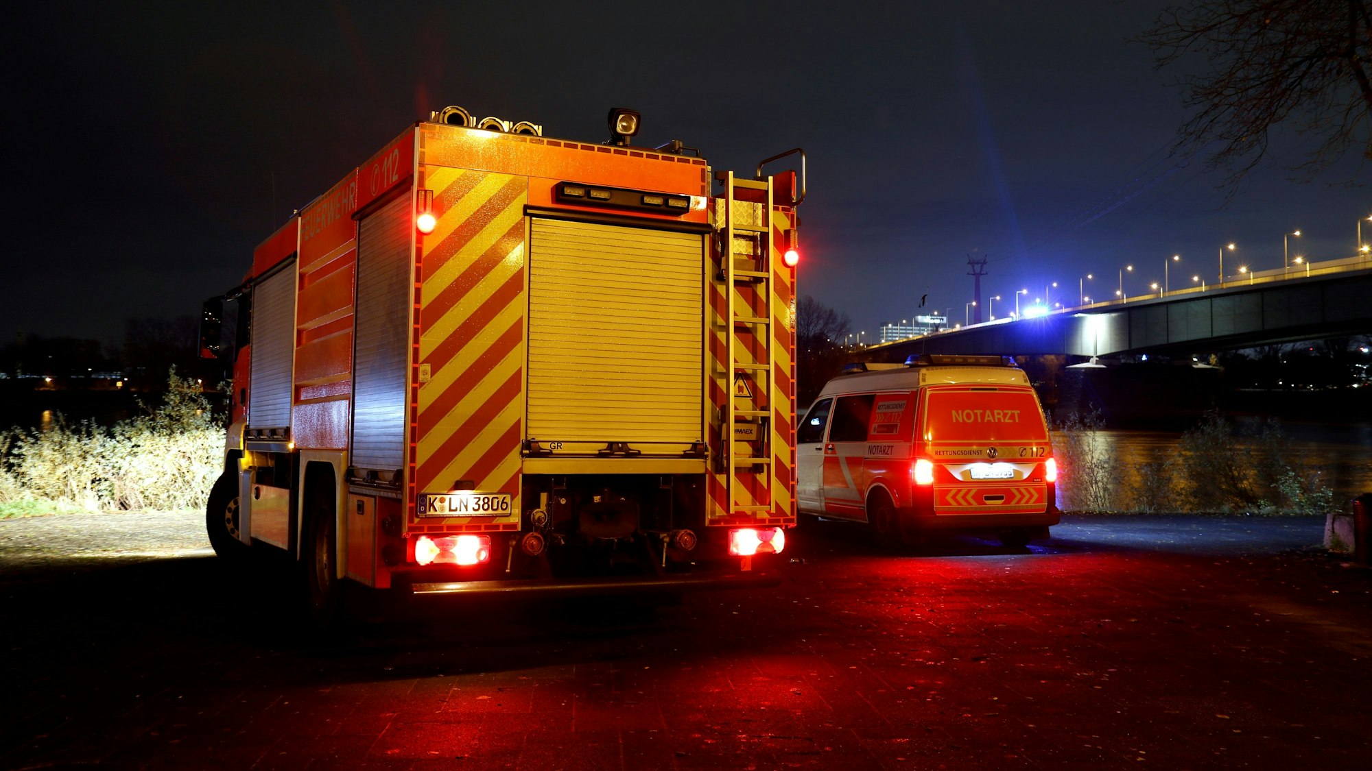 Ein Löschfahrzeug und ein zweites Einsatzfahrzeug stehen in der Nacht unterhalb einer Brücke.