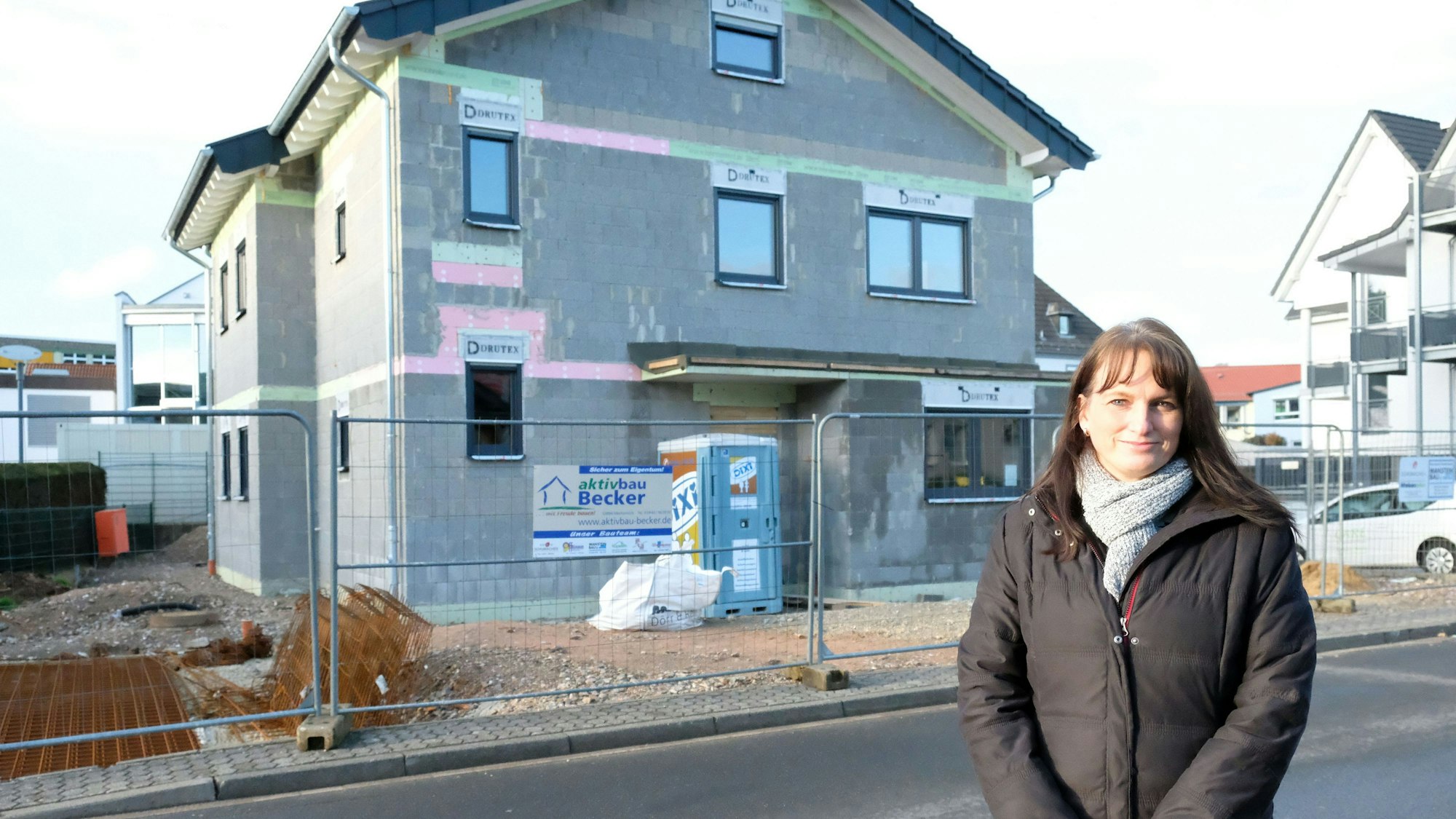 Birgit Junctorius steht vor dem Neubau ihres Wohnhauses in der Straße "Am Hammerwerk" in Kall. Es ist deutlich zu sehen: Dort hinter dem Bauzaun ist noch Baustelle.