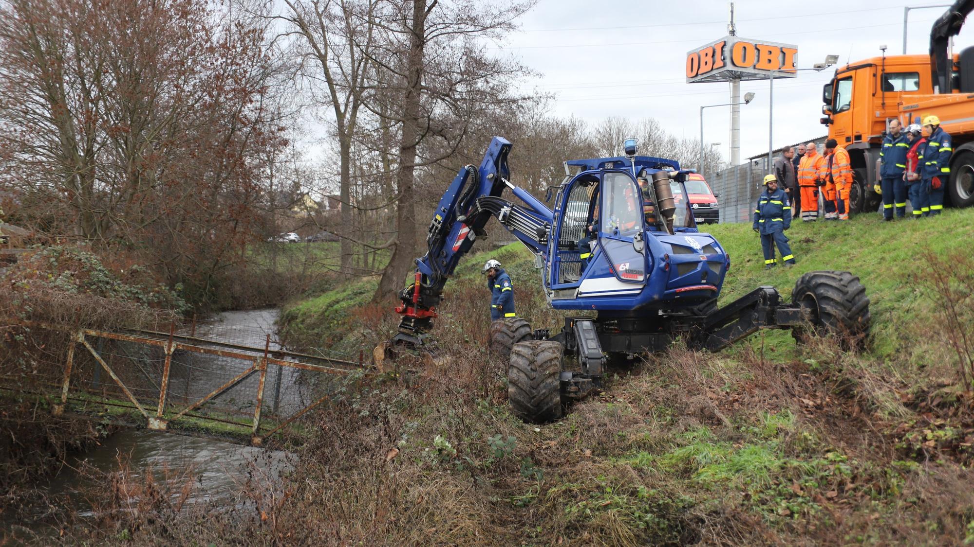 Ein blauer Bagger entfernt eine Brücke über einem Graben.