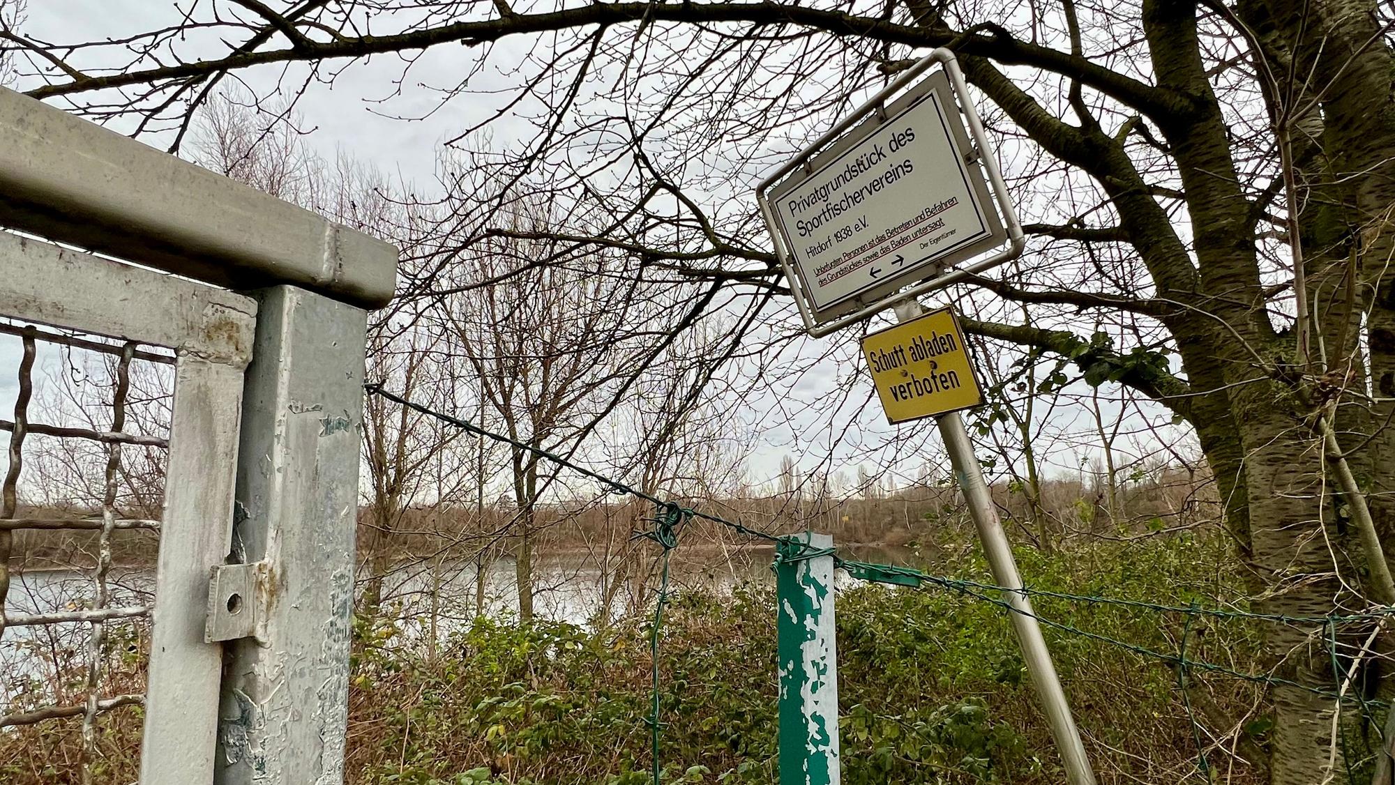 Tor und Zaun mit Verbotsschildern am bewaldeten Seeufer
