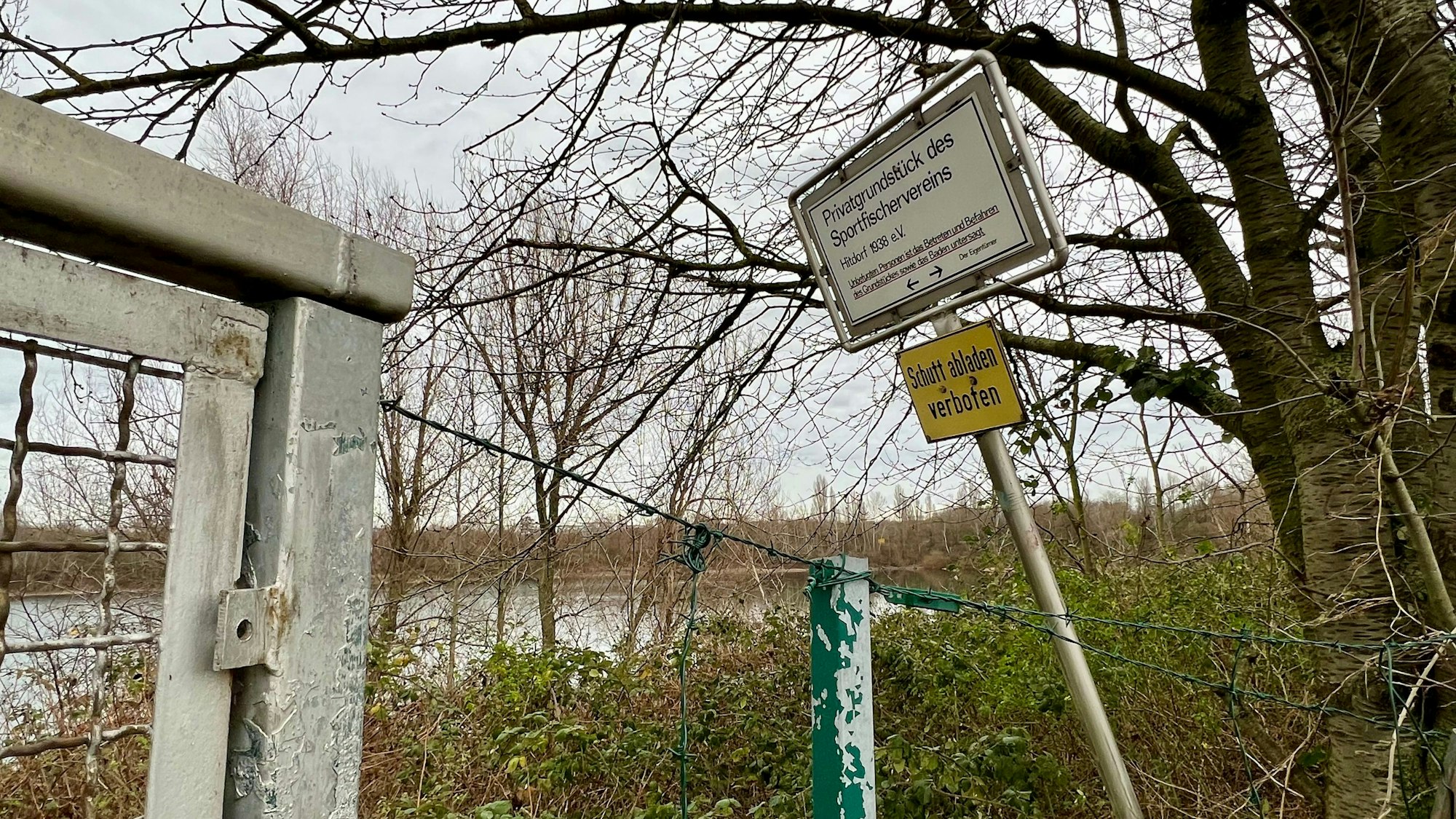 Tor und Zaun mit Verbotsschildern am bewaldeten Seeufer