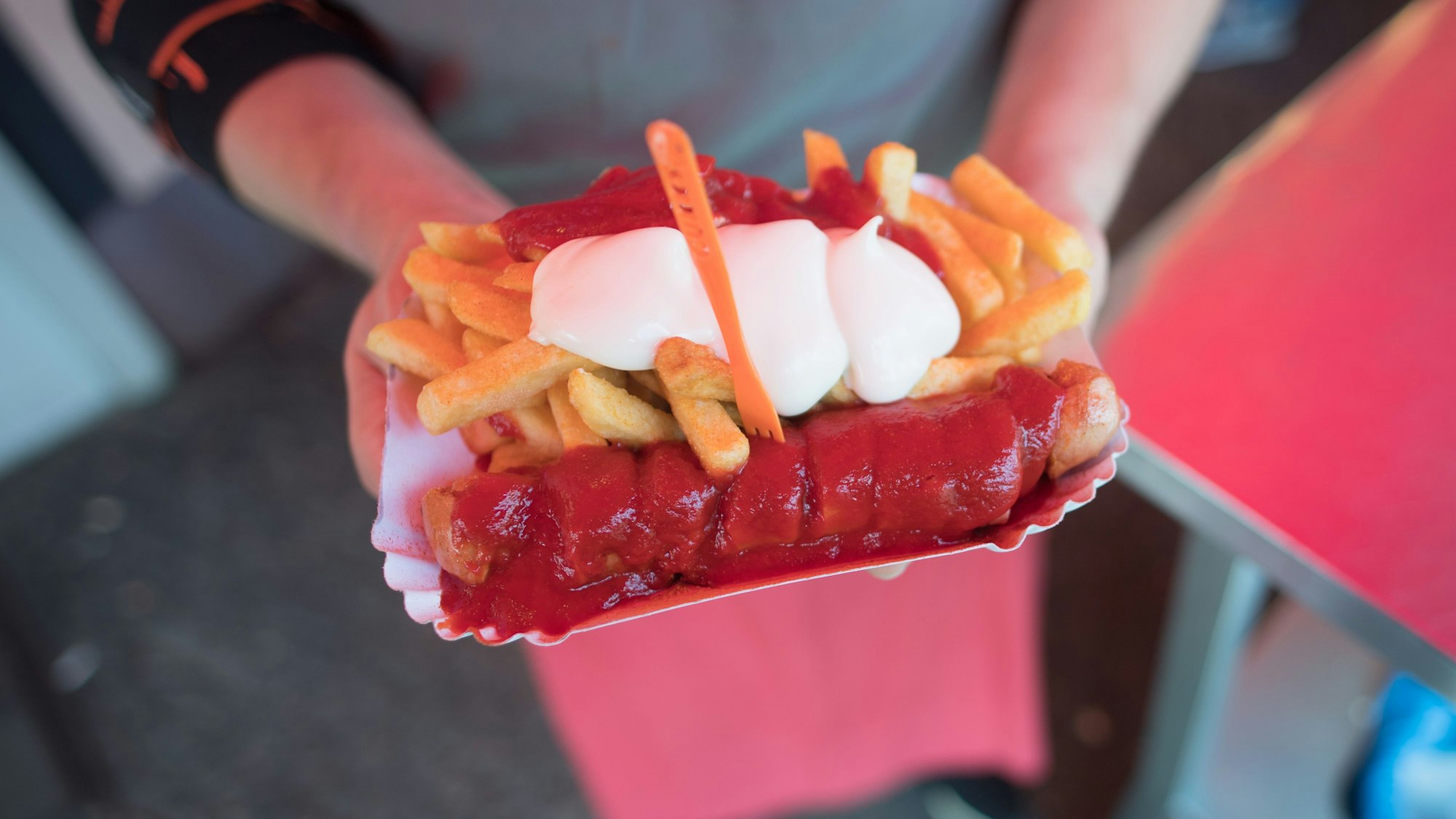 Ein Mann hält eine Currywurst in einem Schälchen mit Pommes.