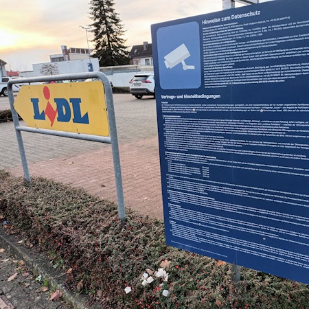 Ein großes, blaues Schild mit sehr langem, kleingedrucken Text steht an der Einfahrt zum Lidl-Parkplatz in Lohmar. Hier wird über Datenschutz, Vertrags- und Einstellbedingungen informiert.
