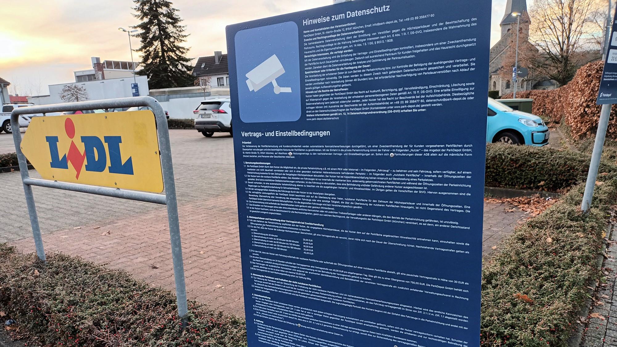 Ein großes, blaues Schild mit sehr langem, kleingedrucken Text steht an der Einfahrt zum Lidl-Parkplatz in Lohmar. Hier wird über Datenschutz, Vertrags- und Einstellbedingungen informiert.