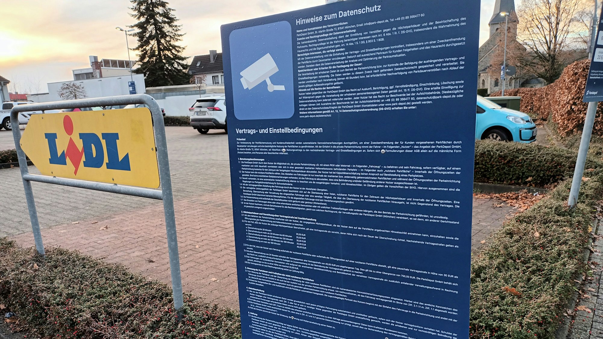 Ein großes, blaues Schild mit sehr langem, kleingedrucken Text steht an der Einfahrt zum Lidl-Parkplatz in Lohmar. Hier wird über Datenschutz, Vertrags- und Einstellbedingungen informiert.