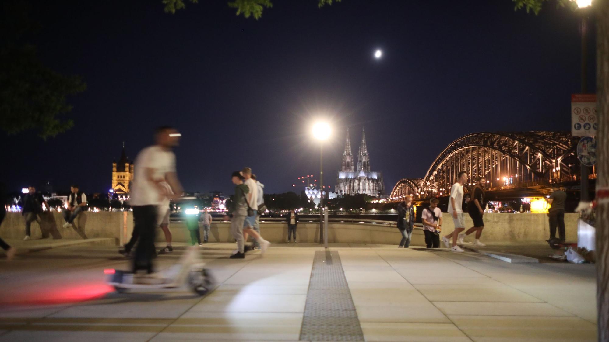 Ein Mann macht eine Nachtfahrt am Rheinboulevard mit einem E-Scooter in Deutz.