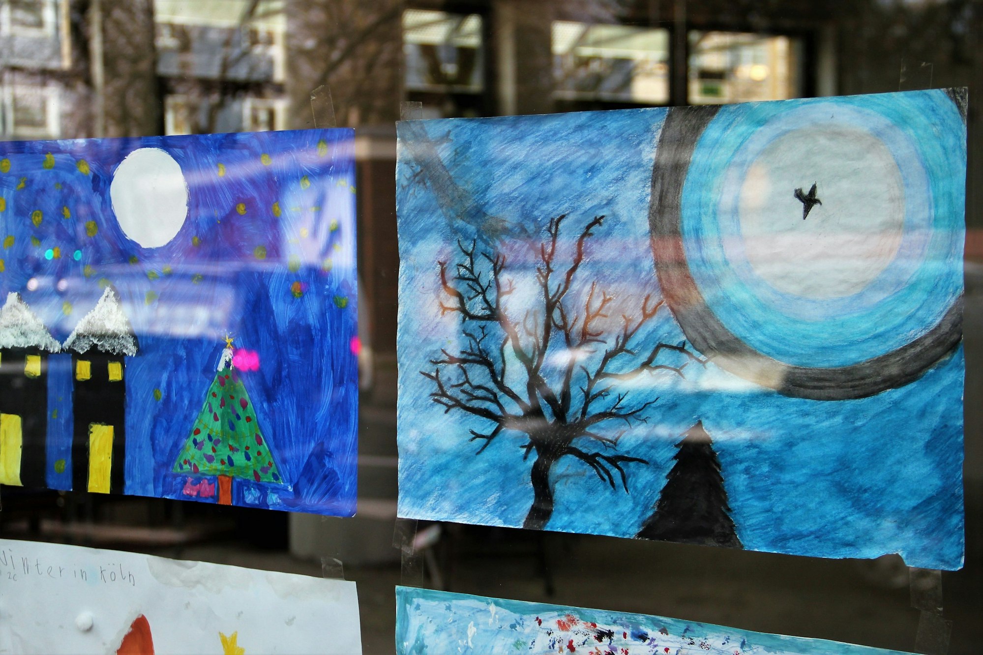 Zwei winterliche Bilder kleben an einer Glasscheibe.