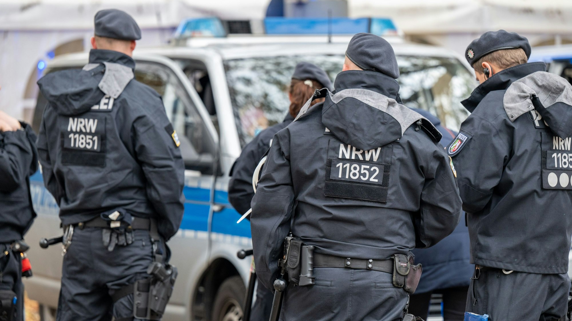 Polizisten und Einsatzfahrzeuge der Polizei von hinten.