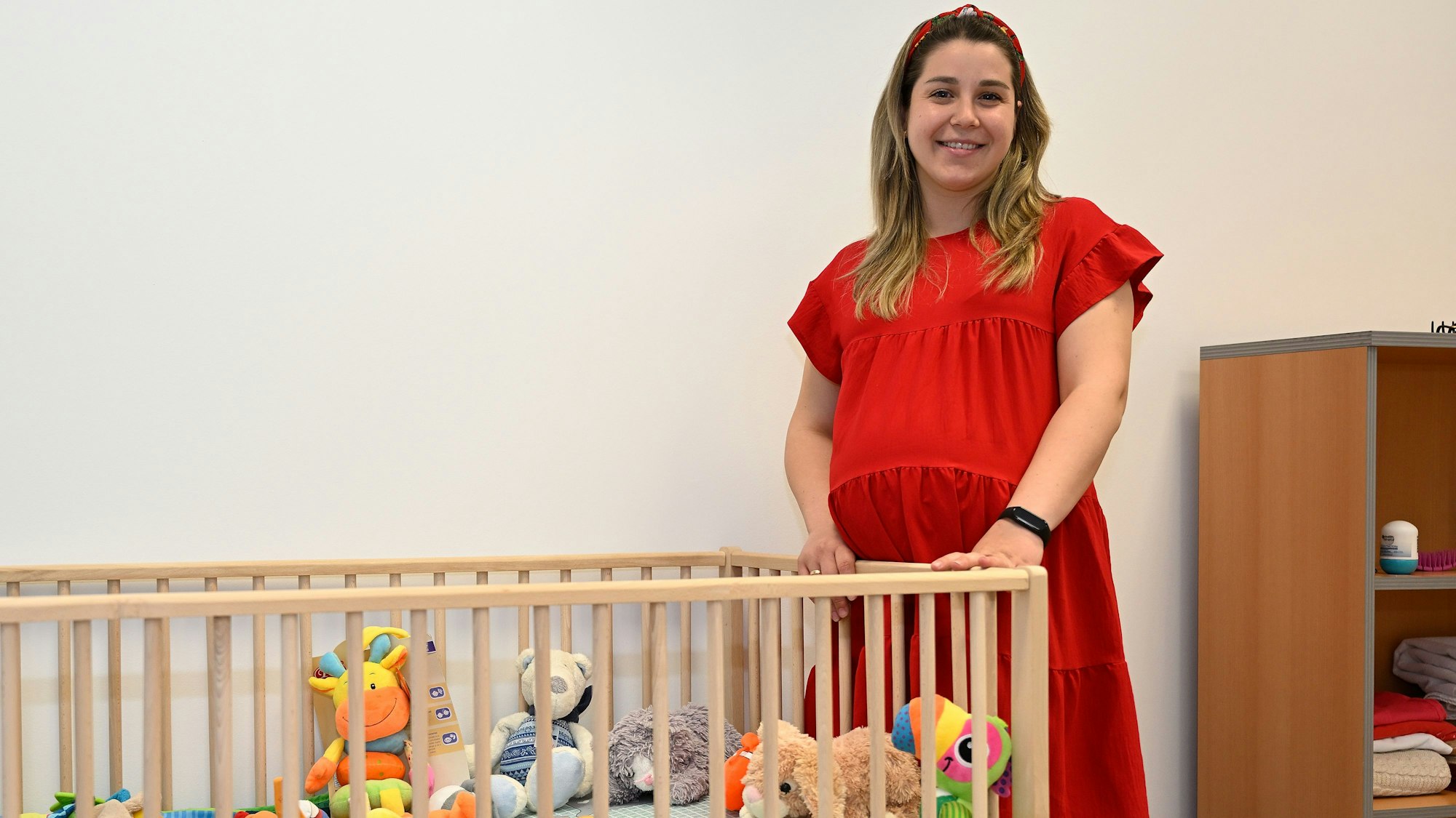 Yulia Zdzozhek (23) steht in einem roten Kleid an einem Kinderbett.