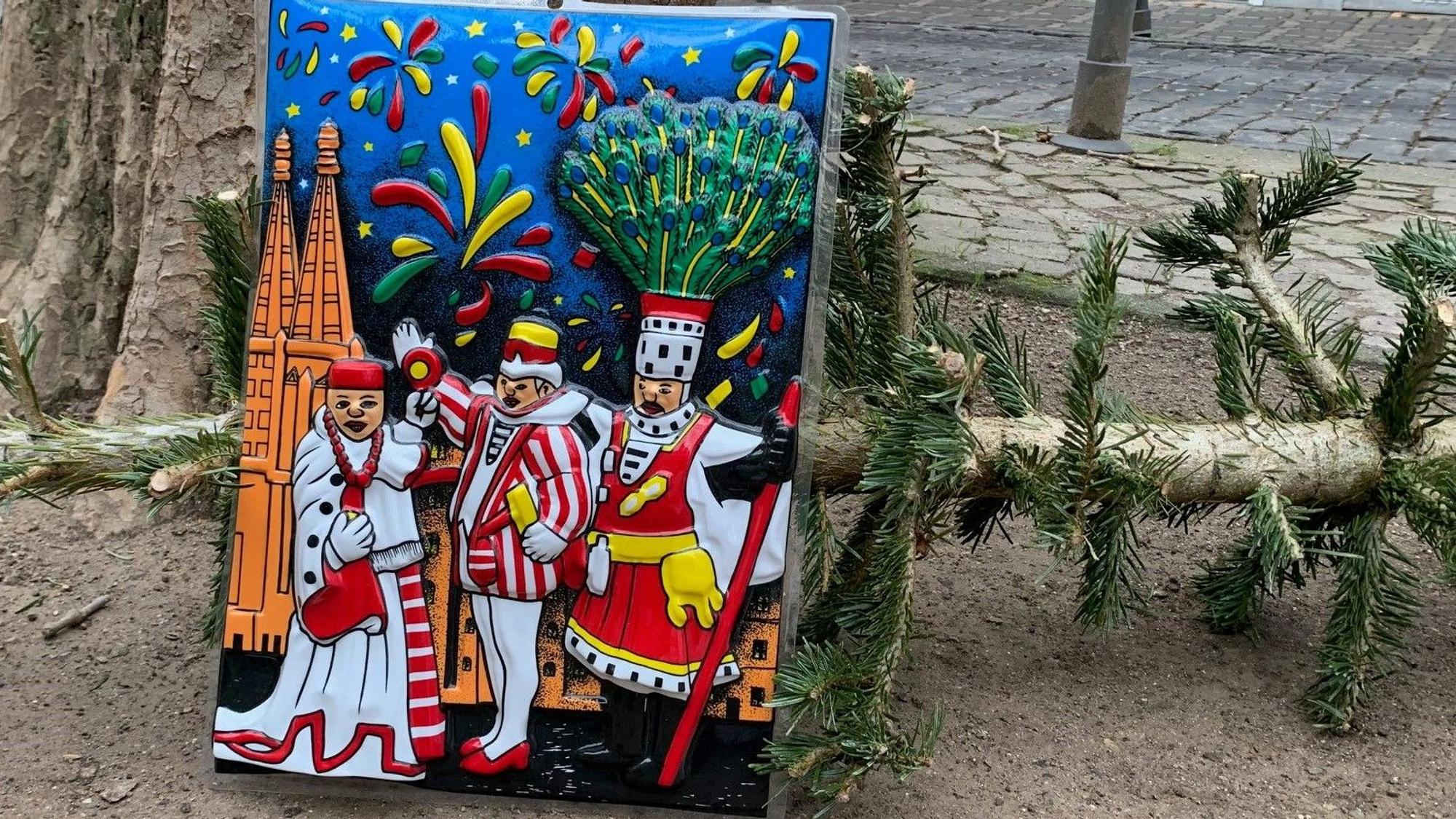 Auf der Weißenburgstraße im Agnesviertel lehnt ein Plastikbild mit dem Kölner Dreigestirn am 30. Dezember 2022 an den Resten eines Weihnachtsbaums.