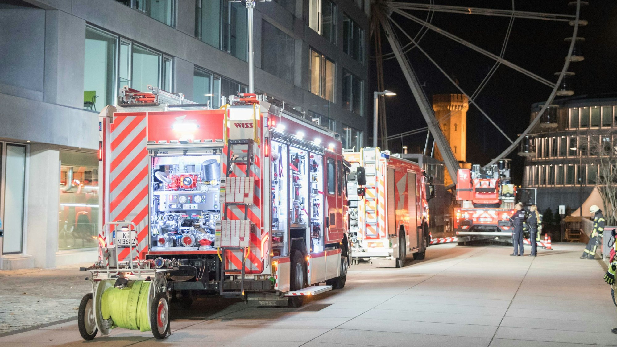Die Kölner Feuerwehr sichert einen Brand in der Straße "Am Zollhafen" im Kölner Rheinauhafen. Im Hintergrund ist das Riesenrad am Schokoladenmuseum zu sehen.