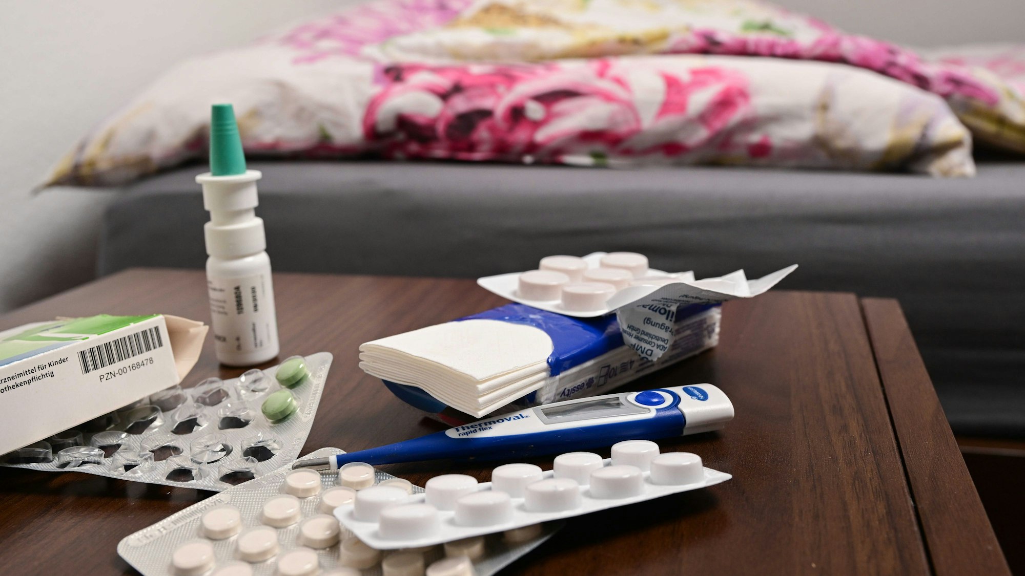 Ein Fieberthermometer und Medikamente liegen auf einem Nachttisch.