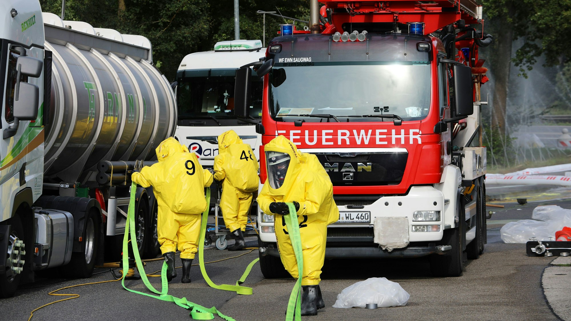 Einsatzkräfte in Schutzanzügen tragen einen Schlauch zu havarierten Tanklastzug.