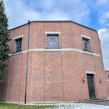 Ein nahezu runder Fachwerkbau mit dunkler Tür und Fenstern nur im oberen Bereich steht in winterlicher Landschaft.