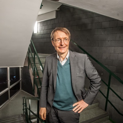 Karl Lauterbach steht in einem Treppenhaus, er schaut an der Kamera vorbei.