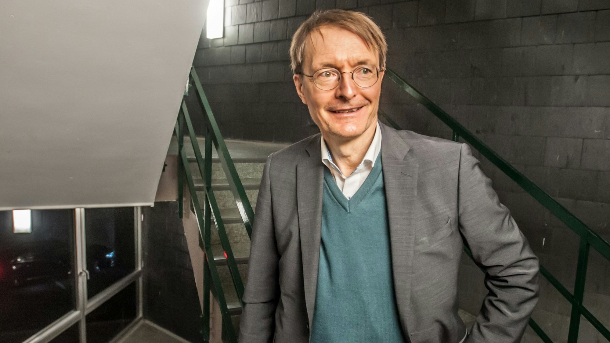 Karl Lauterbach steht in einem Treppenhaus, er schaut an der Kamera vorbei.