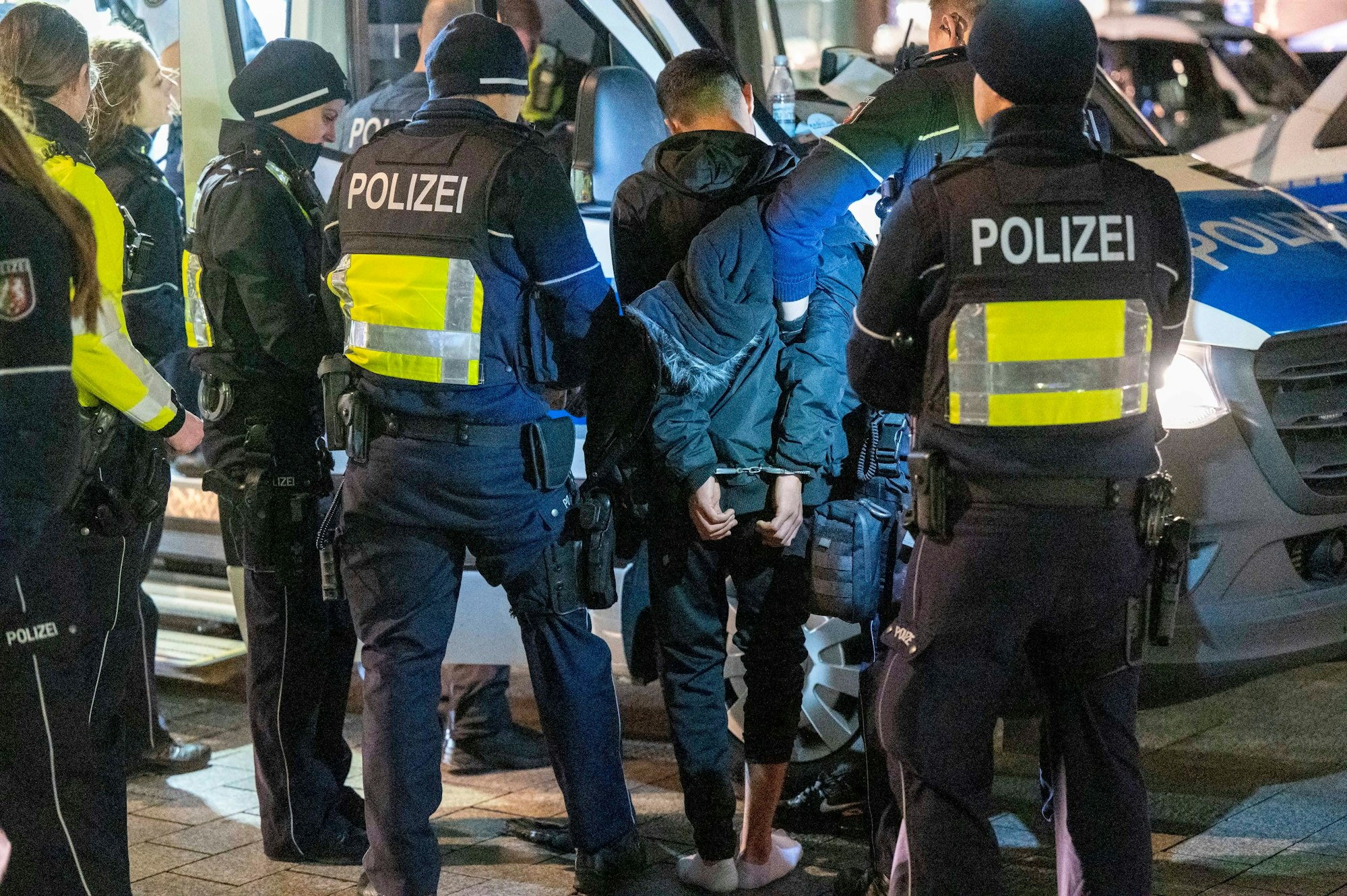 Polizisten haben einem jungen Mann die Hände auf den Rücken gefesselt.