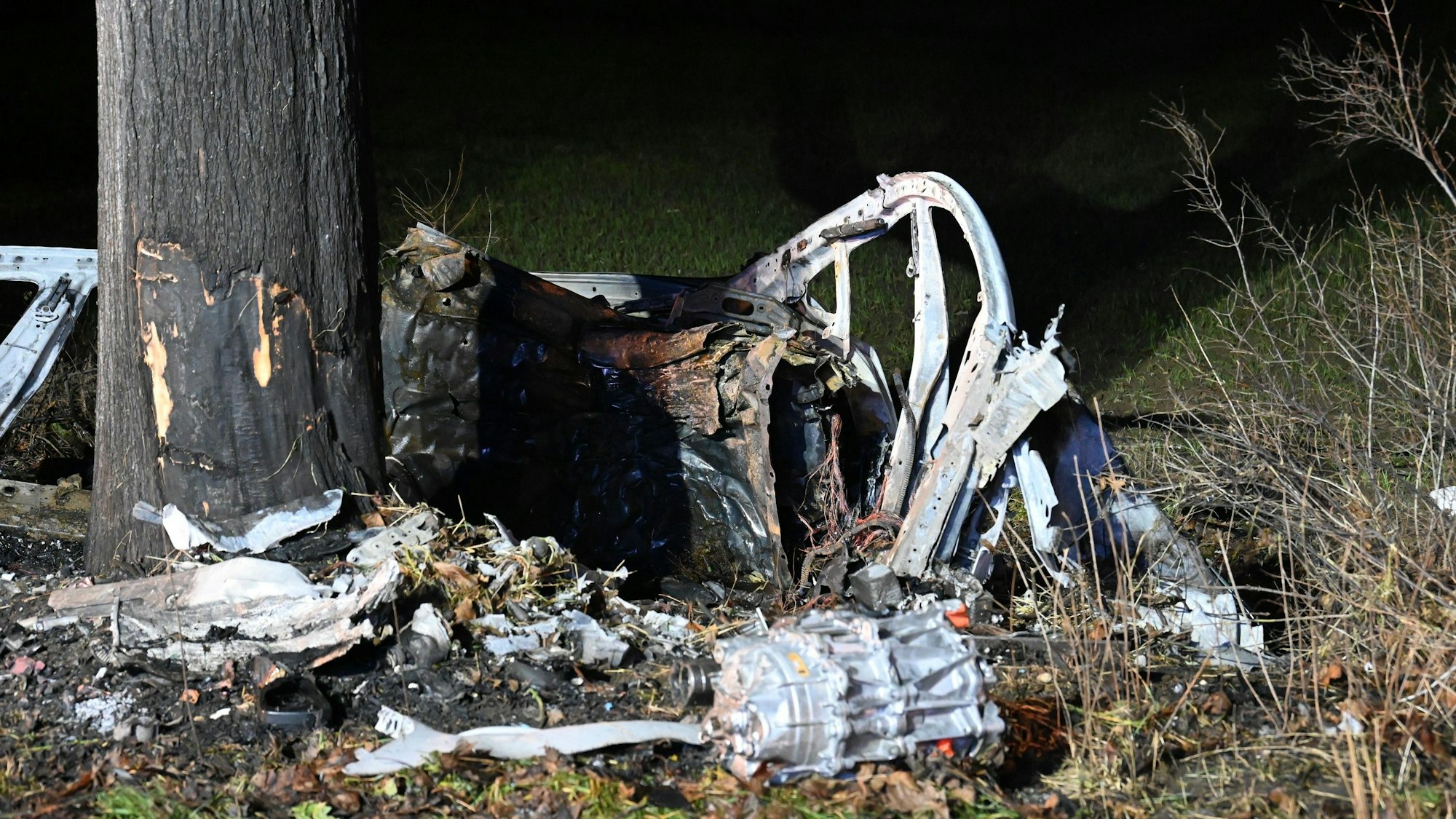 Zwischen Bergheim und Pulheim ist ein Tesla am 31.12.2022 auf der L213 ausgebrannt. Überreste des Wagens liegen am Straßenrand, daneben steht ein Baum.