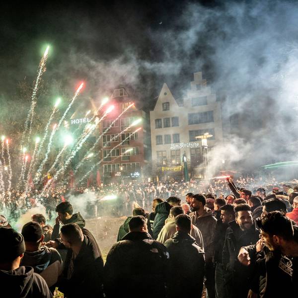 Böller und Feuerwerk explodieren in der Kölner Altstadt. Eine Menschenmenge, fast ausschließlich Männer, schaut zu.