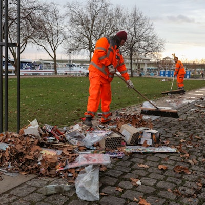 Zwei Mitarbeiter der AWB kehren den Silvestermüll am Rheingarten in der Altstadt zusammen.