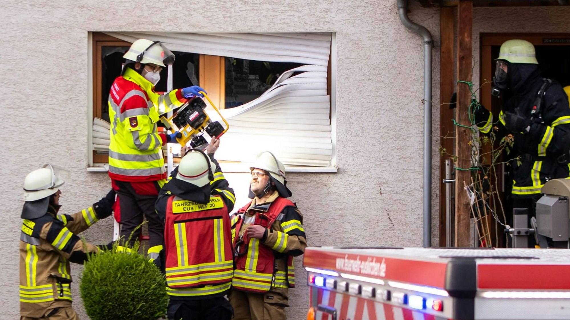 Feuerwehrleute stehen an einem Haus, in dem es gebrannt hat.