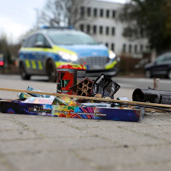 Feuerwerksreste liegen auf einem Gehweg an der Bergisch Gladbacher Hauptstraße. Dahinter fährt ein Polizeiauto auf der Straße.