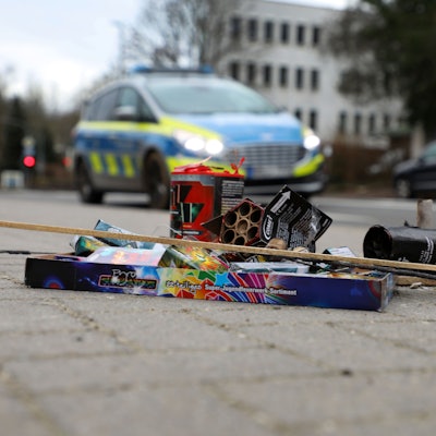 Feuerwerksreste liegen auf einem Gehweg an der Bergisch Gladbacher Hauptstraße. Dahinter fährt ein Polizeiauto auf der Straße.