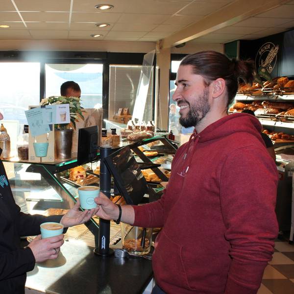Zwei Mitarbeiter im Laden mit Recup Mehrwegbechern in der Hand.
