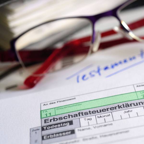 Ein Formular für die Erbschaftsteuererklärung sowie Brille und Testament liegen auf einem Tisch.