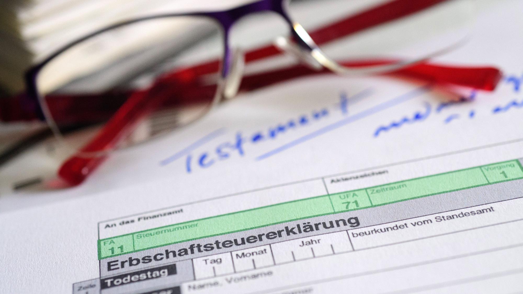 Ein Formular für die Erbschaftsteuererklärung sowie Brille und Testament liegen auf einem Tisch.
