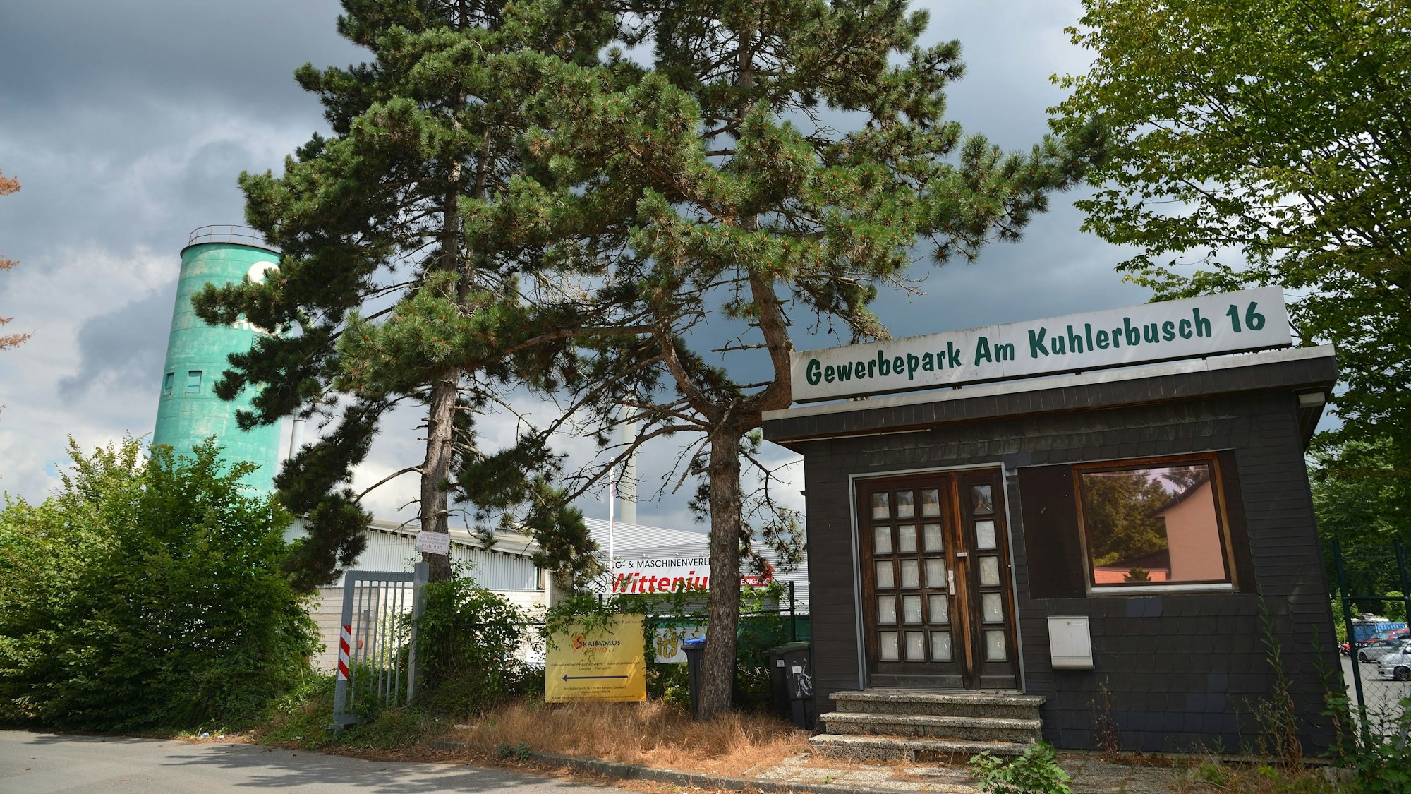 Ein Gebäude mit der Aufschrift „Gemwerbepark Am Kuhlerbusch 16“ neben einem Baum, im Hintergrund sind Firmengebäude zu sehen.