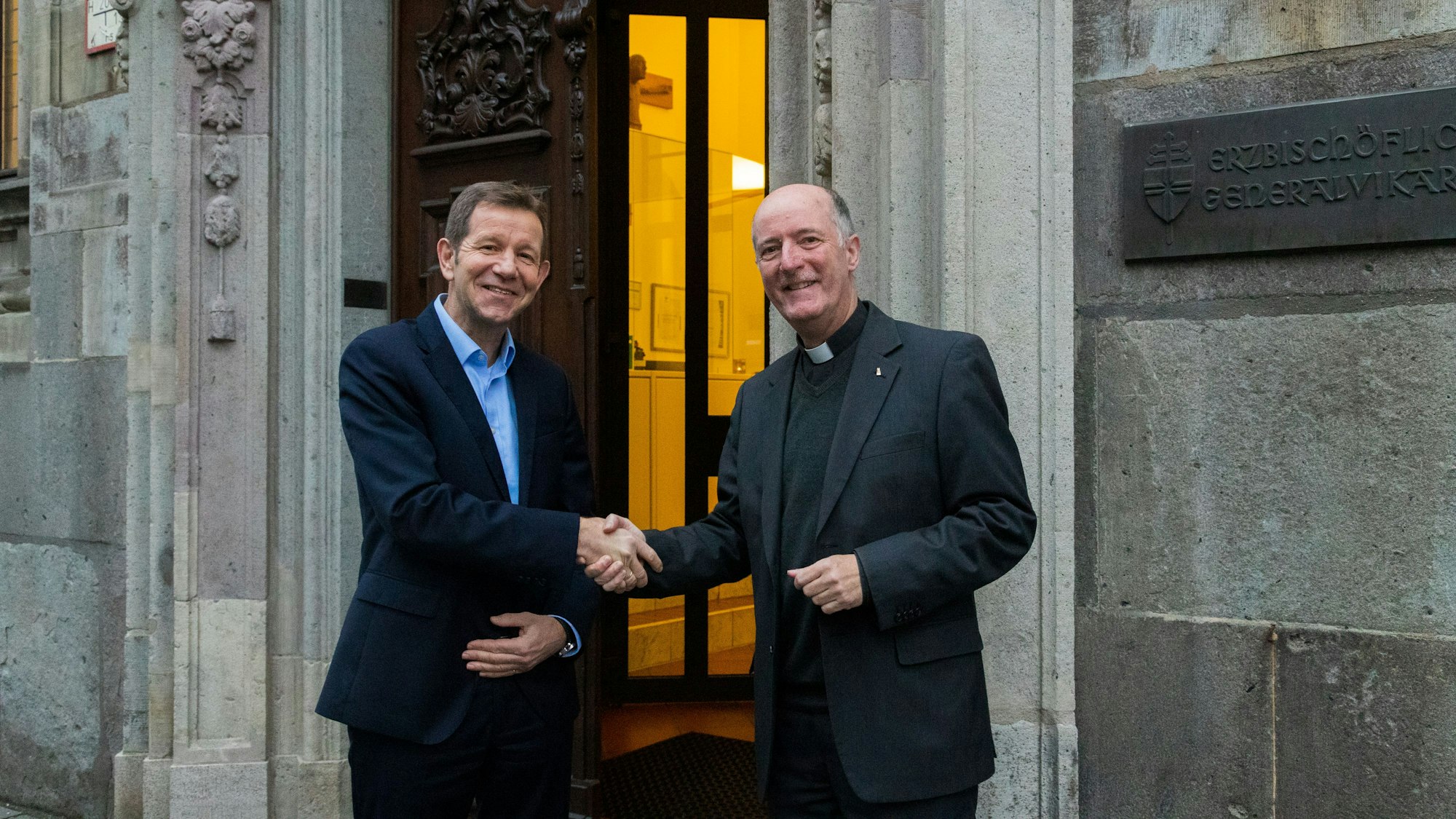 Zwei Männer stehen vor dem Eingang und geben sich die Hand