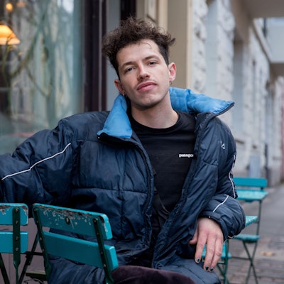 Paul Köninger sitzt auf einem Stuhl. Er trägt eine blaue Jacke und hat seinen rechten Arm auf der Armlehne eines zweiten Stuhls.