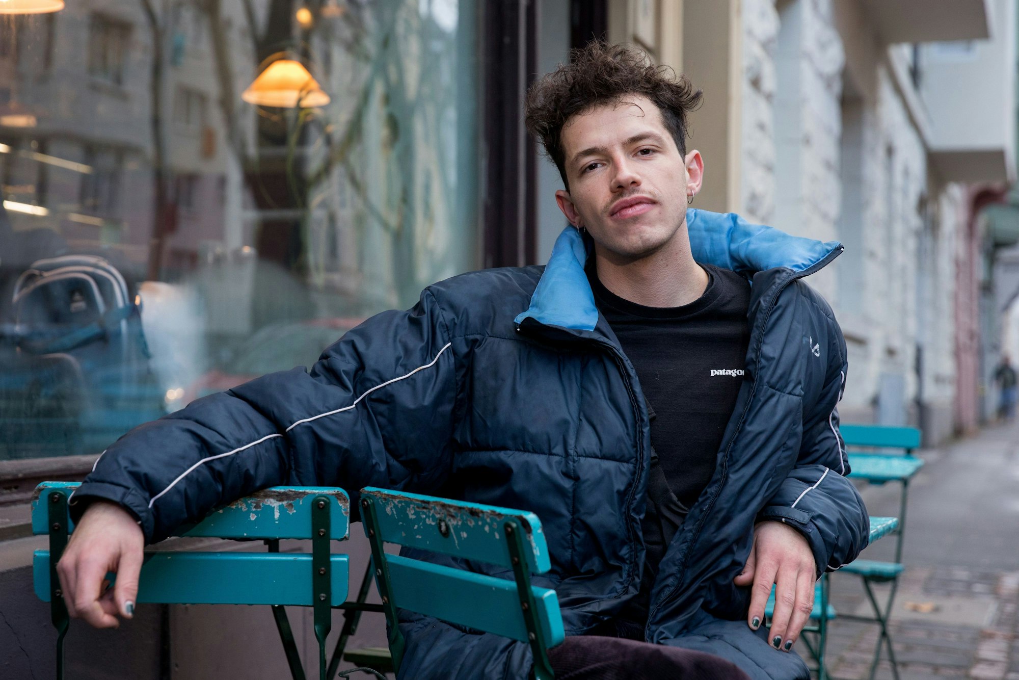 Paul Köninger sitzt auf einem Stuhl. Er trägt eine blaue Jacke und hat seinen rechten Arm auf der Armlehne eines zweiten Stuhls.