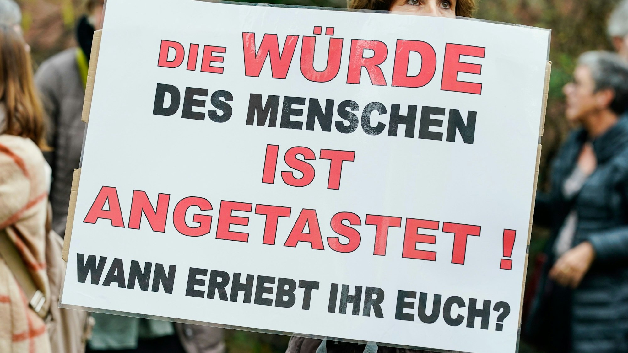 Eine Frau hält in einer Protest-Demonstration in Weinheim (Baden-Württemberg) ein Plakat in den Händen, auf dem steht: „Die Würde des Menschen ist angetastet! Wann erhebt ihr euch?“