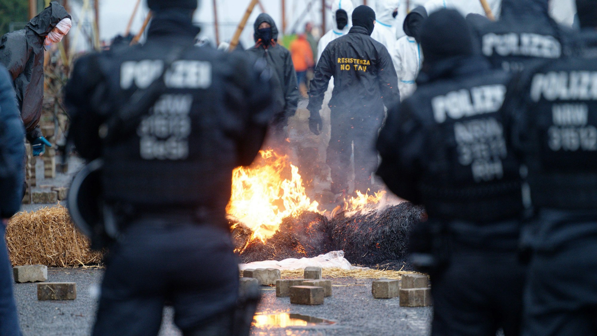 Polizisten und Klimaschützer stehen sich in Lützerath an einer brennenden Barrikade gegenüber.